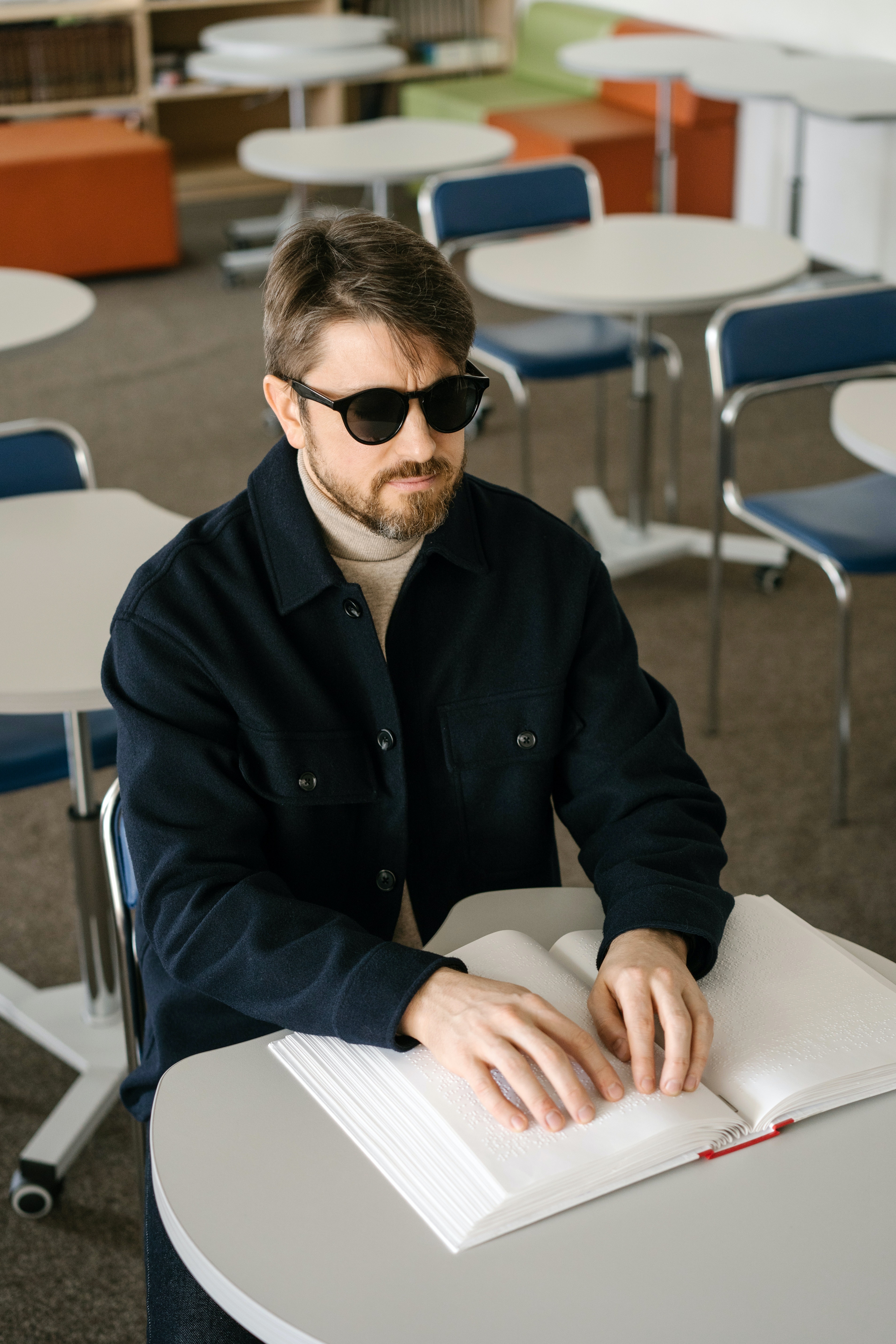 A student sitting in a classroom, reading a braille book on a table