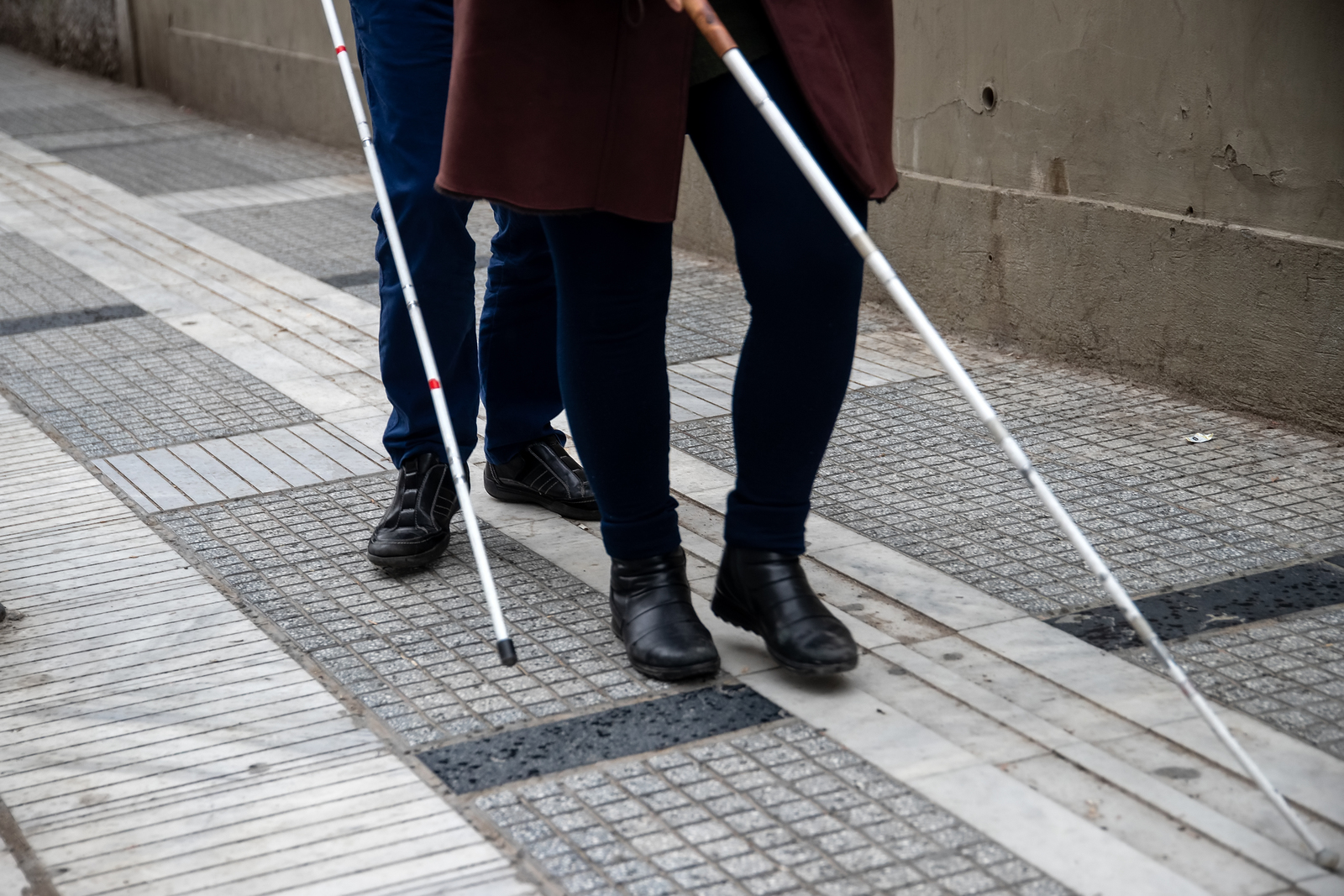 A couple walking down a path, both of them are using white canes, and talking.